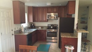 A compact kitchen with wooden cabinets, a stainless steel refrigerator, a microwave, and an oven.