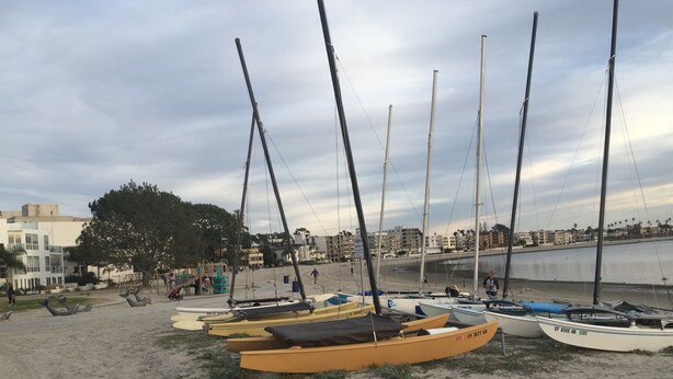 A sandy beach with several boats moored in the sand, a playground, and buildings in the background.