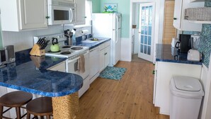 A kitchen with white cabinets, a blue marble countertop, a wooden floor, and a ceiling fan. - Newly Remodeled 2 Bedroom Cottage On The Beach. The Kaitlyn Cottage (Clinton)
