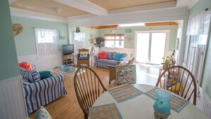 A spacious living room with a dining area, a television, and a large window. - Newly Remodeled 2 Bedroom Cottage On The Beach. The Kaitlyn Cottage (Clinton)