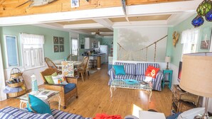 A cozy living room with a sofa, chairs, a dining table, and a kitchen in the background. - Newly Remodeled 2 Bedroom Cottage On The Beach. The Kaitlyn Cottage (Clinton)