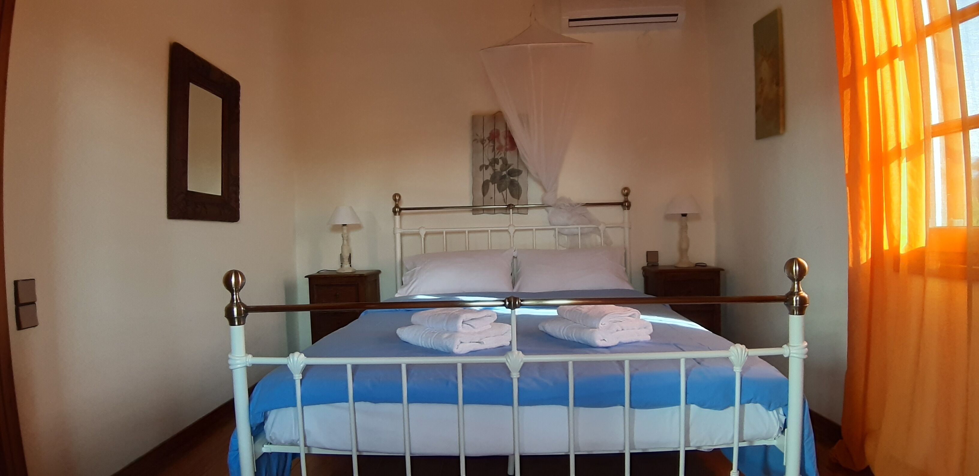 Una cama bien hecha con sábanas blancas y una colcha de cuadros azules y blancos. Junto a la cama hay una mesita de noche blanca con una lámpara.