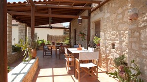An outdoor patio with a wooden table and chairs, surrounded by potted plants and stone walls.