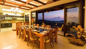 Un espace repas avec une grande table dressée pour le repas, un lustre et une vue sur l’extérieur.