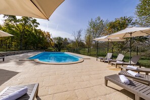 A swimming pool with lounge chairs and umbrellas, surrounded by a stone patio and trees.