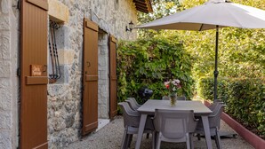 Un patio al aire libre con una mesa, sillas, una puerta de madera con la inscripción 'Gîte du Pigeonnier' y una parrilla.