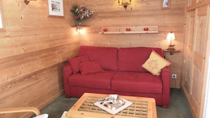 Una habitación acogedora con un sofá rojo, una pequeña mesa de madera con una bandeja y luces fijadas a la pared.