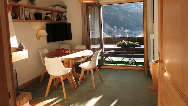 Una habitación acogedora con una mesa de comedor, sillas, un televisor y un balcón con vistas a un paisaje nevado.