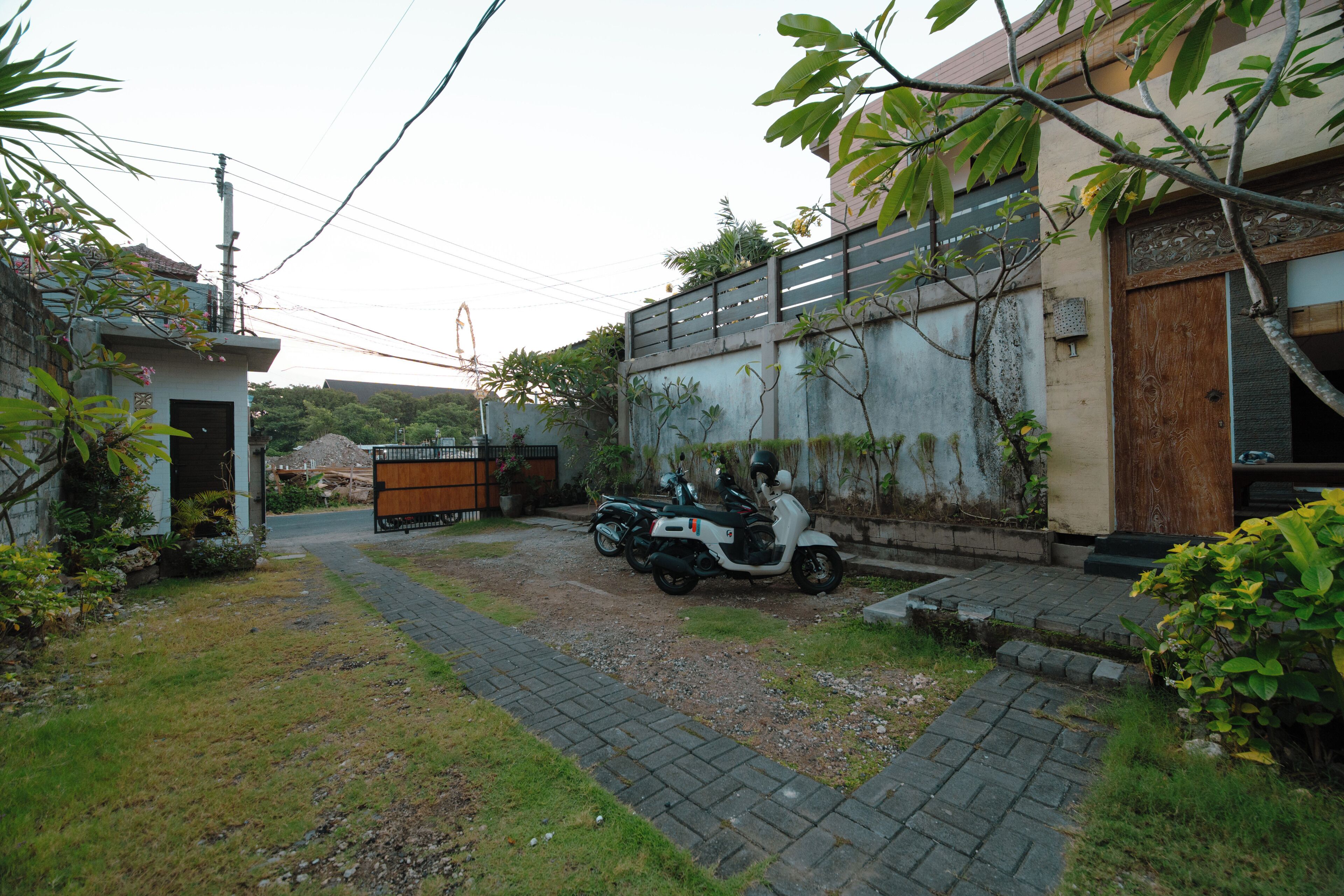 A paved driveway leading to a gated entrance with a parked scooter.