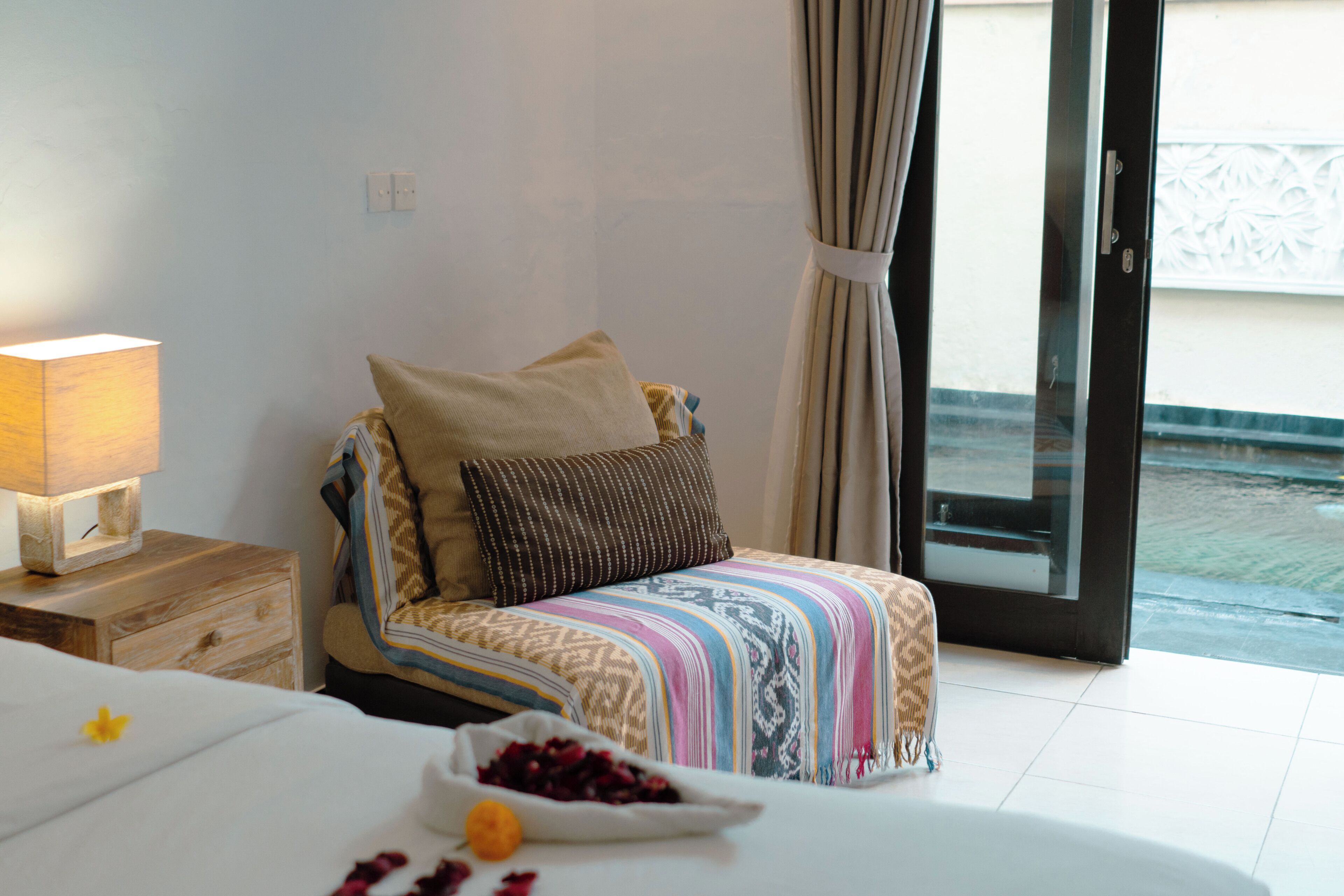 A bedroom with a bed, a bedside table with a lamp, a window with curtains, and a view outside.