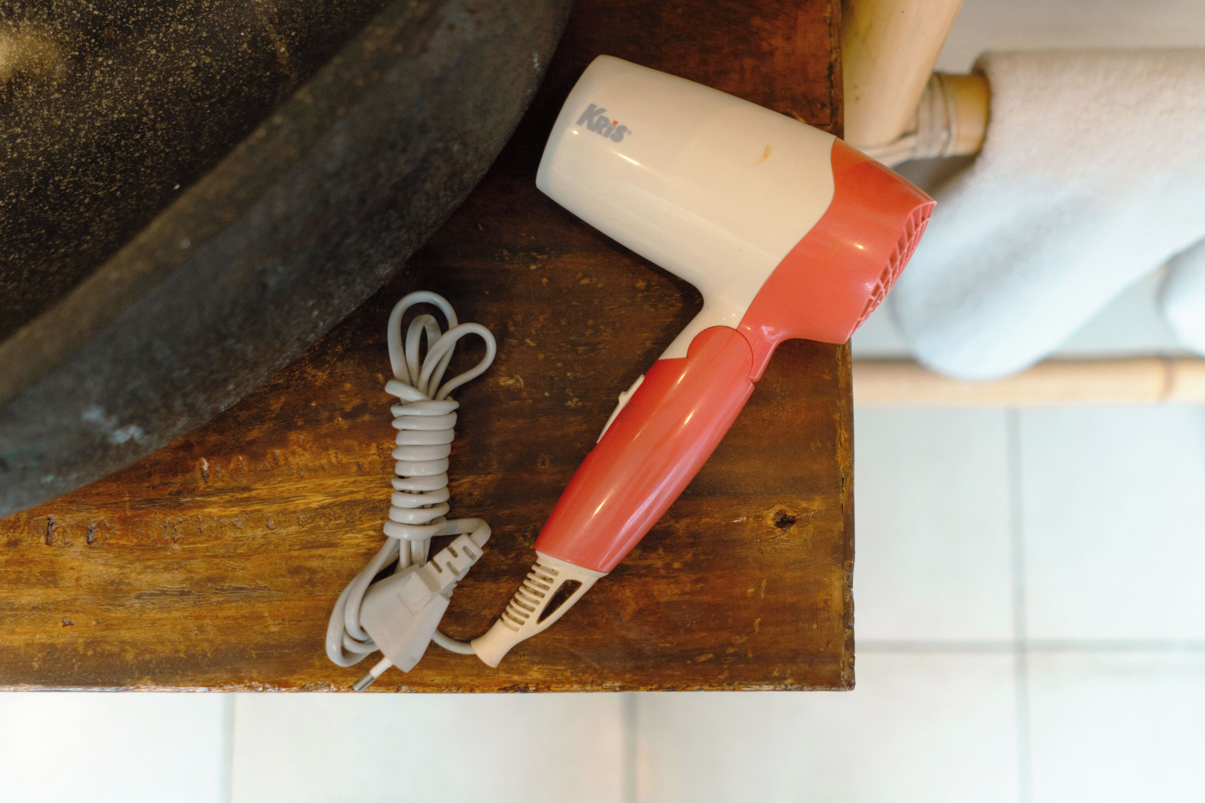 A hair dryer with a cord and a plug on a wooden surface.
