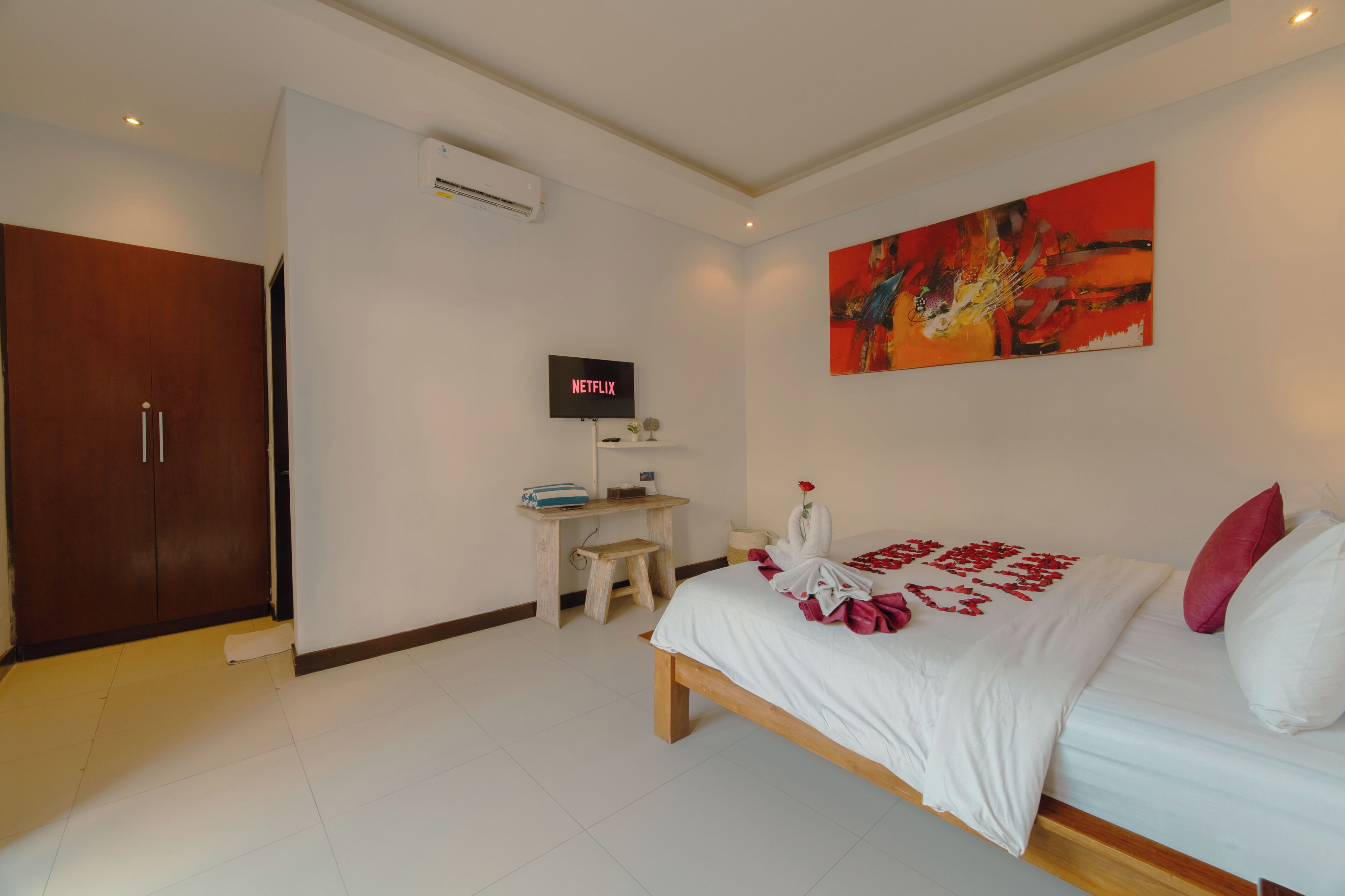 A hotel room with a bed, a desk with a computer, a wardrobe, and a painting on the wall.