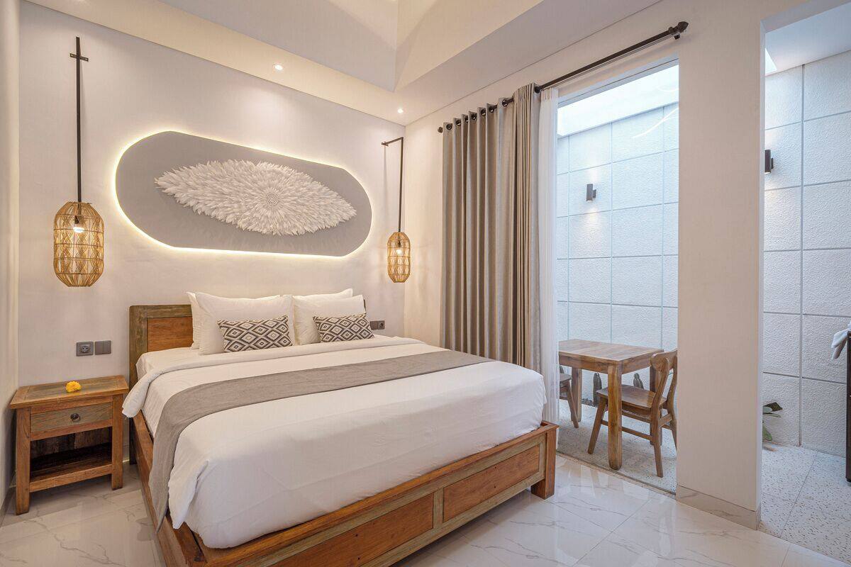 Quarto moderno com cama grande, mesas de cabeceira, luminária na parede e vista através de uma porta deslizante.