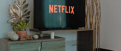A flat-screen TV on a wooden stand with a decorative leaf and a potted plant beside it.