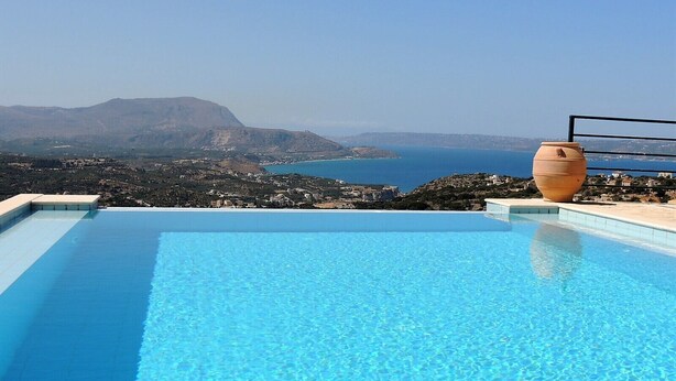 A clear blue infinity pool with a view of the sea and mountains.