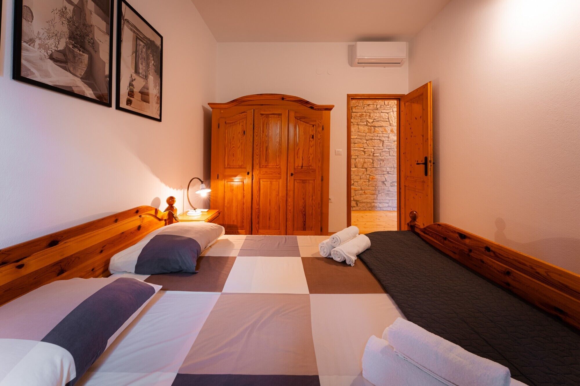 Una habitación con dos camas, un armario de madera, una pared de piedra y una puerta.