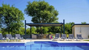 Une piscine entourée d’arbres, avec des chaises longues et une pergola.