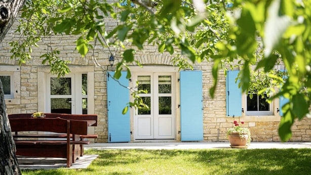 Un bâtiment en pierre avec des volets bleus, un banc et un pot de fleurs.