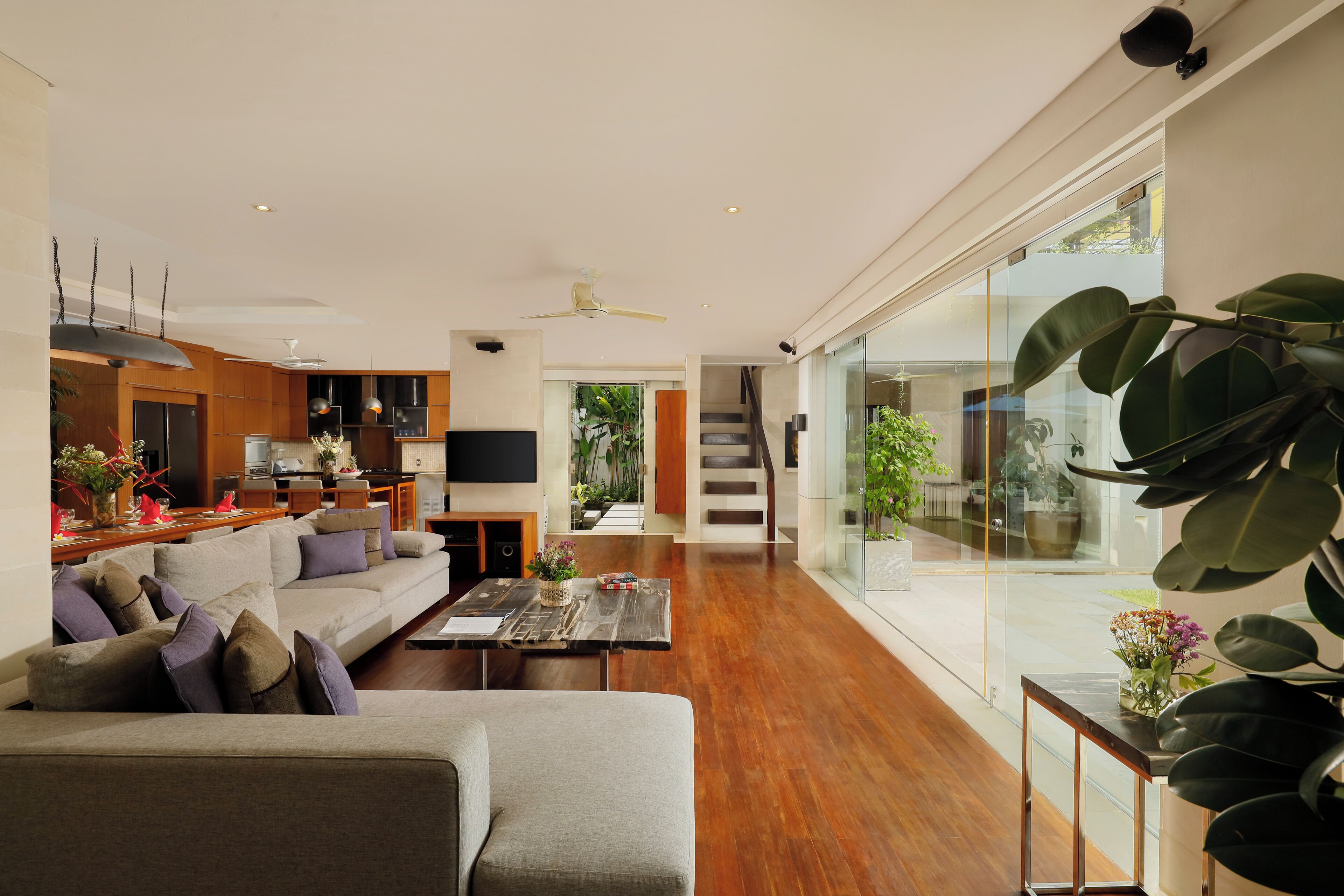 Una sala de estar moderna con sofá, mesa de centro y televisor. Se ve una escalera que sube a un balcón con plantas.