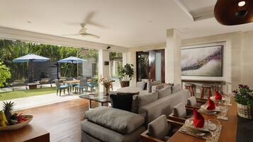 A modern living room with a large sofa, dining table set for four, and a view of the garden through large windows.