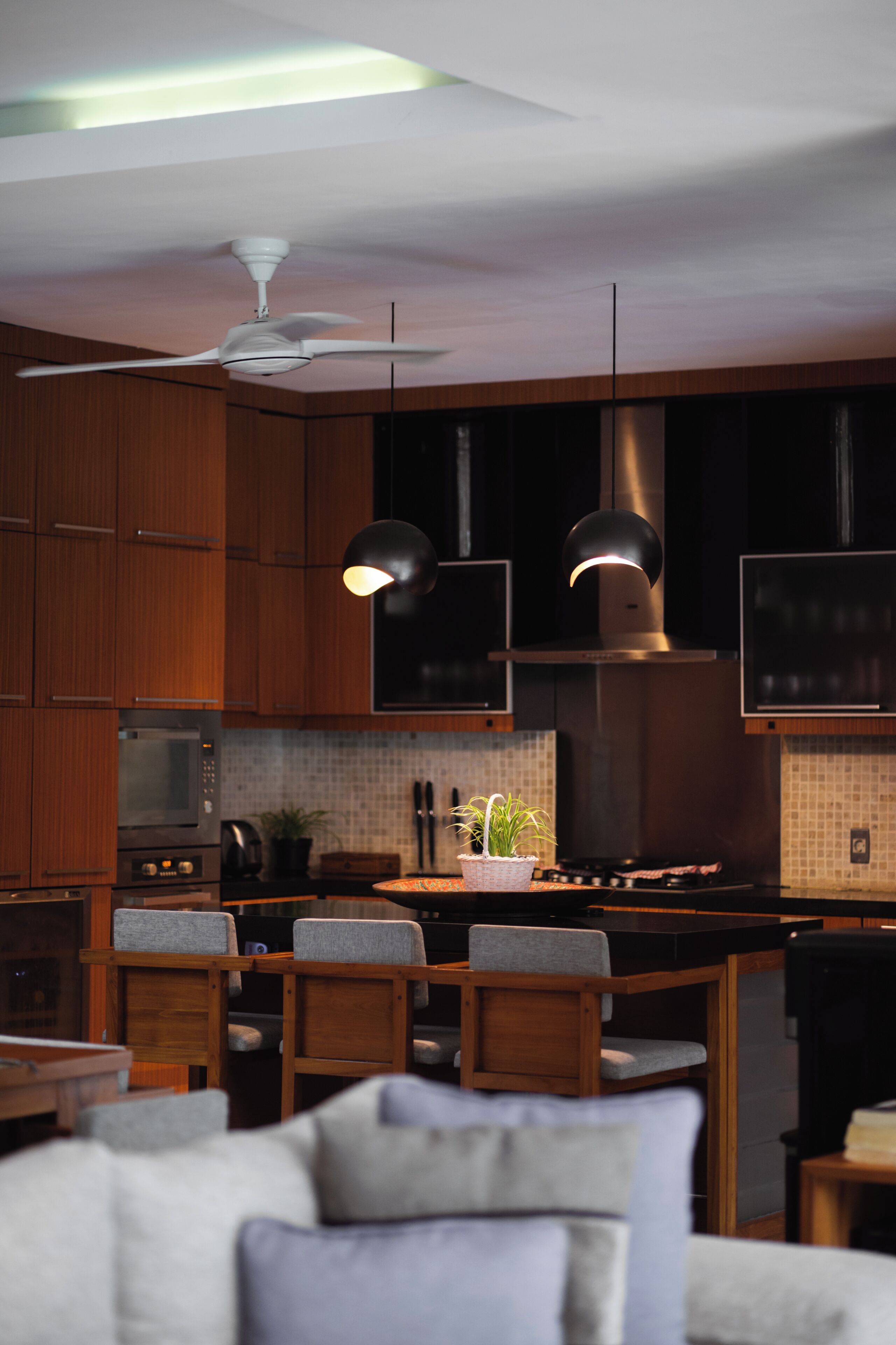 Una cocina moderna con armarios de madera, una isla central, dos lámparas colgantes y un ventilador de techo.