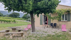 A house with a large tree in the front yard, outdoor seating, and a vineyard in the background. - Cottage "Cherry" to METHAMIS (Méthamis)