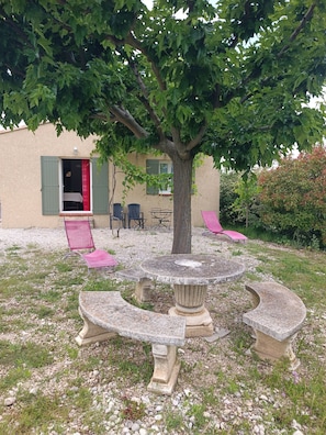 Relax in a serene outdoor space with a stone table and benches, surrounded by a tree and comfortable seating areas.