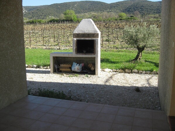 An outdoor stone structure with a chimney, surrounded by a gravel area and a vineyard in the background. - Cottage "Cherry" to METHAMIS (Méthamis)