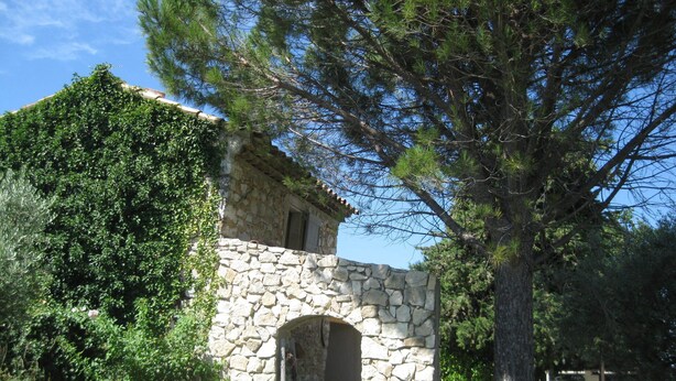 A stone building with a rustic archway, surrounded by lush greenery and pine trees. - Cottage "Cherry" to METHAMIS (Méthamis)