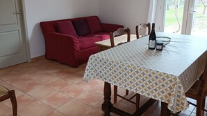 A dining area with a table set for two, a red sofa, and a view through a window. - Cottage "Cherry" to METHAMIS (Méthamis)