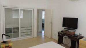 Une chambre à coucher comprenant un lit, une télévision, un bureau et une porte-fenêtre coulissante donnant sur un balcon.