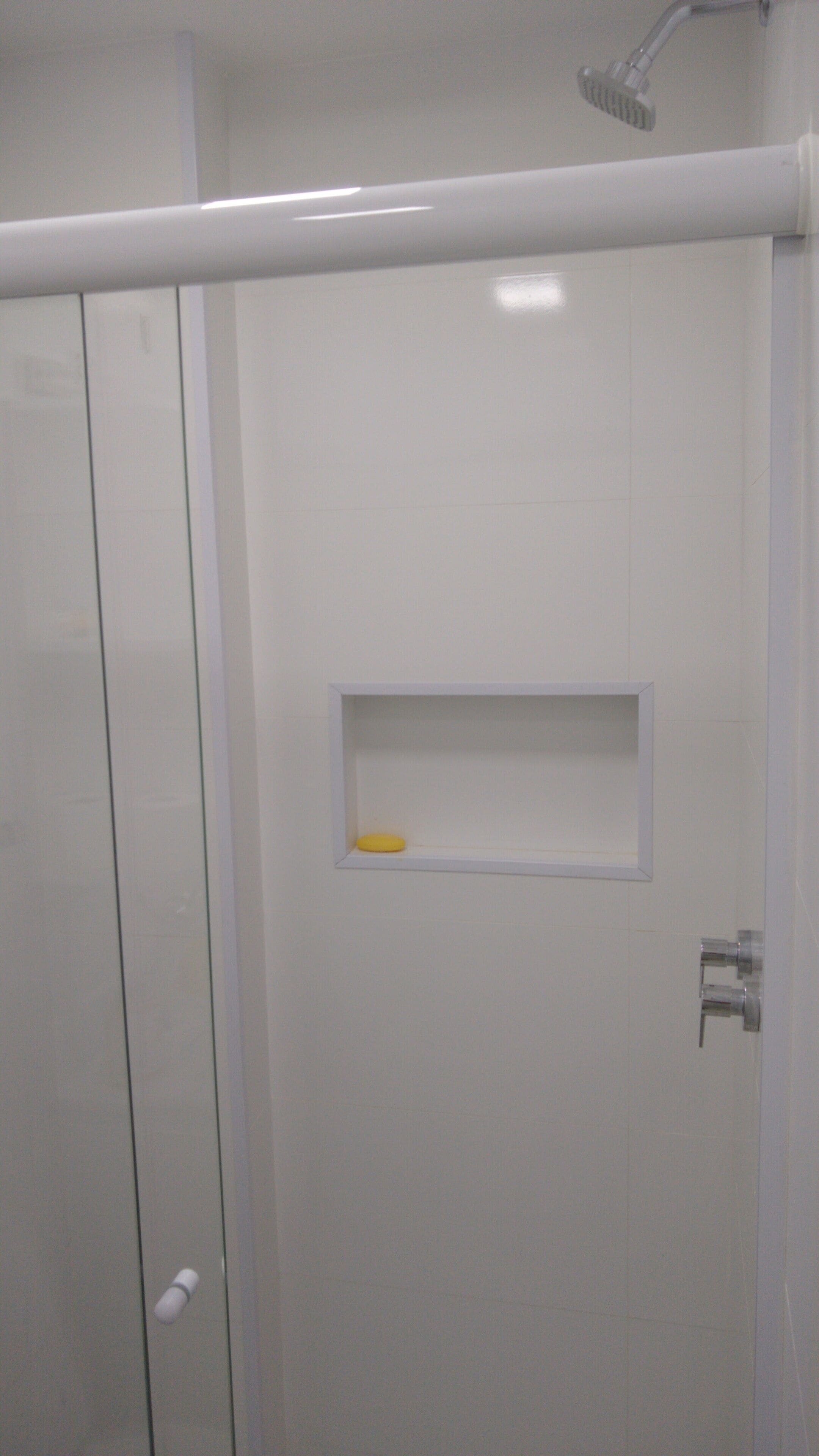 A bathroom with a shower enclosure, a white sink, and a small shelf with a yellow soap bar.