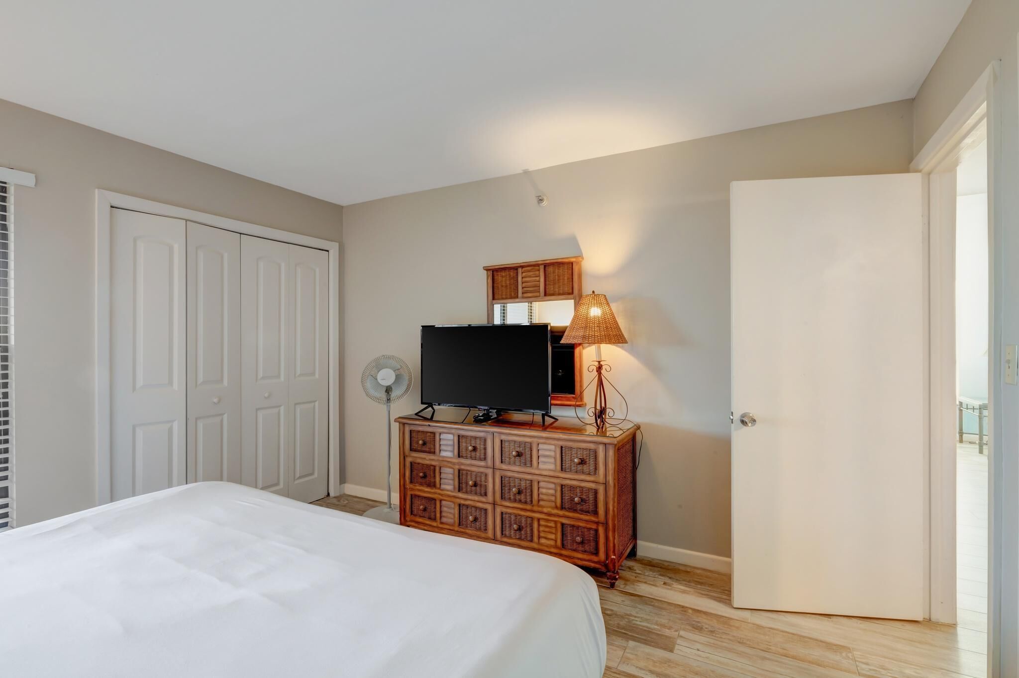 A bedroom with a bed, a dresser with a television, a lamp, and a door.