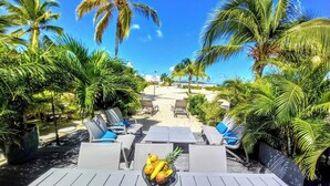 A sunlit outdoor seating area with lounge chairs and a table, surrounded by palm trees and a clear blue sky. - Appartment on the beach, exceptional sea view, condo BORA BORA (Saint-Martin)