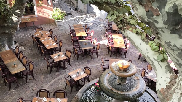 An outdoor café with tables and chairs arranged around a central fountain.