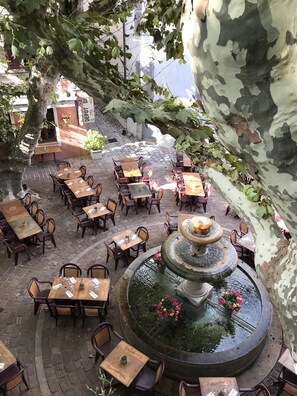Ein Straßencafé mit Tischen und Stühlen, die um einen zentralen Brunnen angeordnet sind.