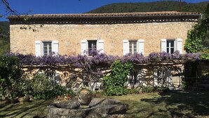 A stone building with white shutters and a garden with purple flowers.