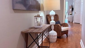 Ein Korridor mit Holzboden, einem Tisch mit einer Laterne, einer Lampe und einem Sessel mit Kissen.