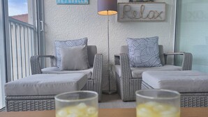 Ein Balkon mit Korbmöbeln, zwei Gläser Orangensaft sowie Wanddekorationen mit den Aufschriften 'NO SHIRT NO SHOES NO PROBLEM' und 'FLIP FLOPS Relax'.