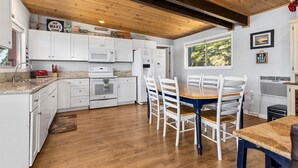 Une cuisine avec des meubles blancs, un plafond en bois et un coin repas comprenant une table et des chaises.