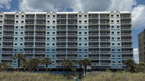 Ein mehrstöckiges Hotel mit Balkonen, ein Sandstrand im Vordergrund und ein bewölkter Himmel.