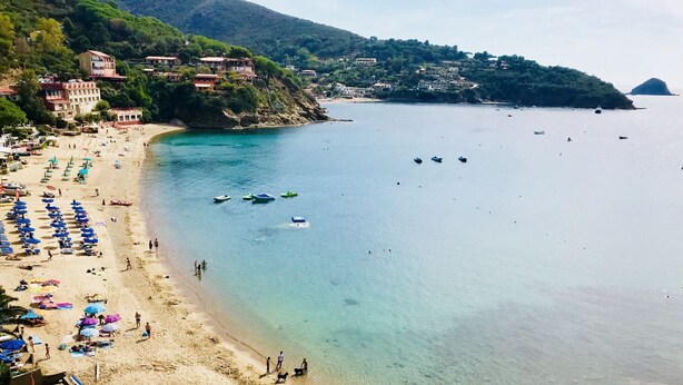 Une plage avec une eau turquoise et limpide, des parasols et des gens.