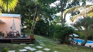 Ein Garten mit einer Holzterrasse, Gartenmöbeln, einem Swimmingpool und üppigem Grün.