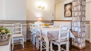 A dining area with a table set for six, surrounded by white chairs, a chandelier, and a bookshelf filled with books. - Beautiful, spacious apartment, five minutes from the castle with air conditioned (Malcesine)
