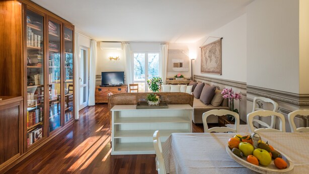 A spacious living area with a wooden bookshelf, a dining table with fruit, a sofa, and a television in the background. - Beautiful, spacious apartment, five minutes from the castle with air conditioned (Malcesine)