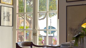A room with a large arched window, a wooden chair, a desk with a vase, and framed artwork on the walls. - CASA OASI with view & terrace (Taormina)