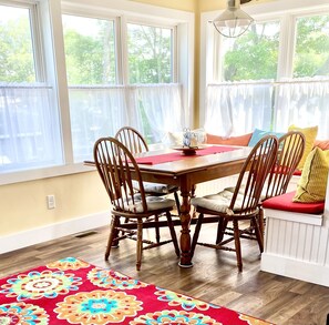Enjoy meals in this cozy dining area with a wooden table and four chairs, surrounded by large windows and a colorful rug.