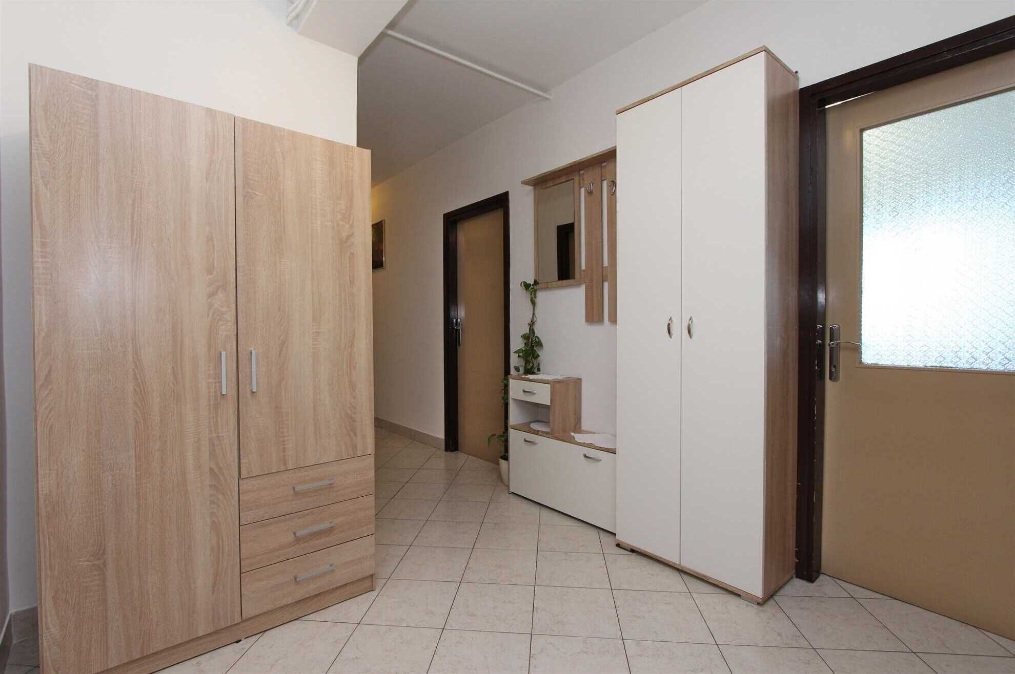 Un couloir avec une armoire en bois, une armoire blanche et une porte dotée d’un panneau en verre dépoli.