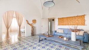 A living room with a blue sofa, a coffee table, a decorative wall hanging, and a patterned floor.
