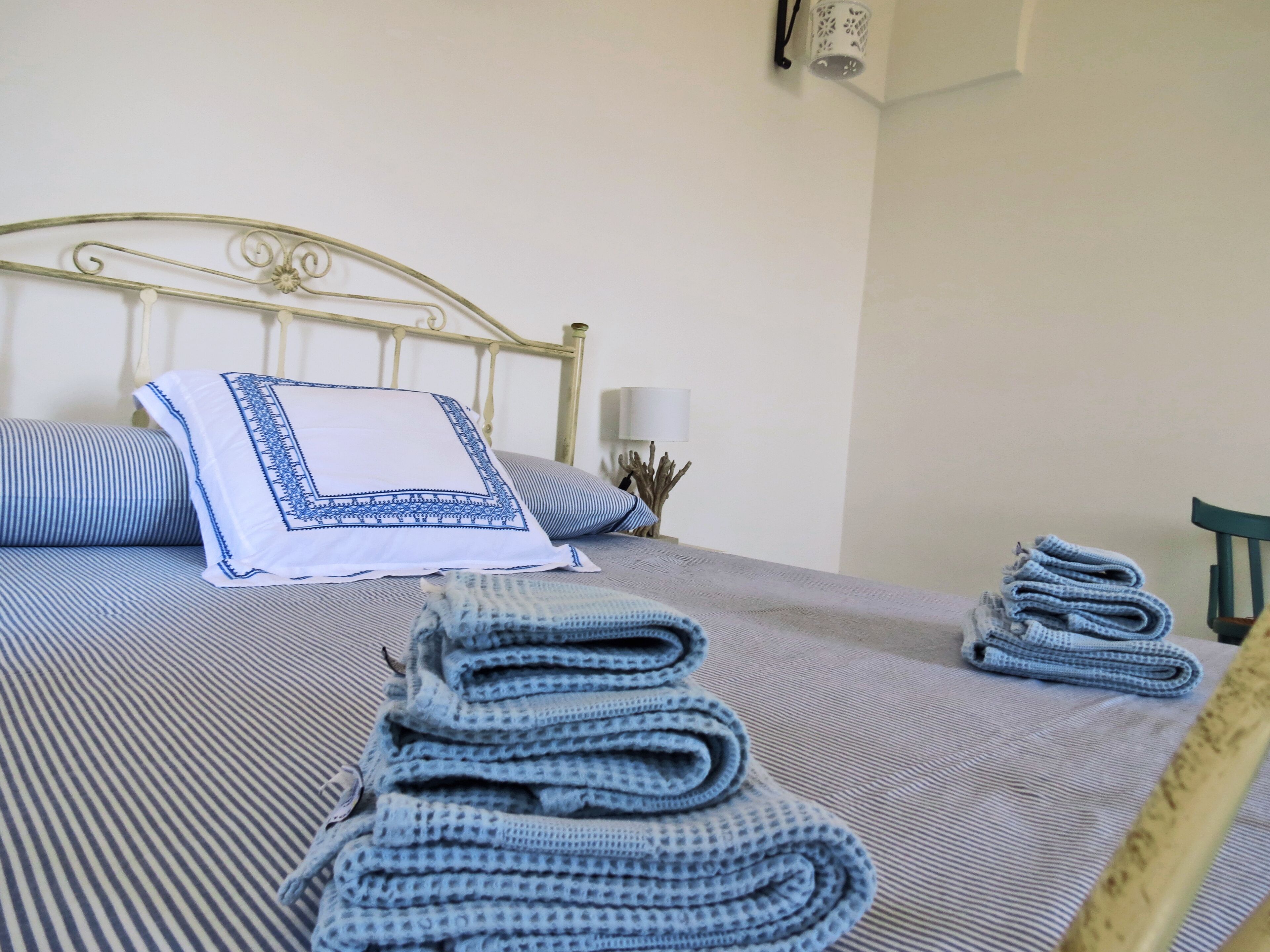 A neatly made bed with a striped bedspread, a white pillow with blue trim, and a folded blanket.